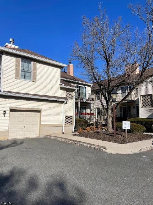 view of front facade featuring an attached garage, a chimney, and aphalt driveway