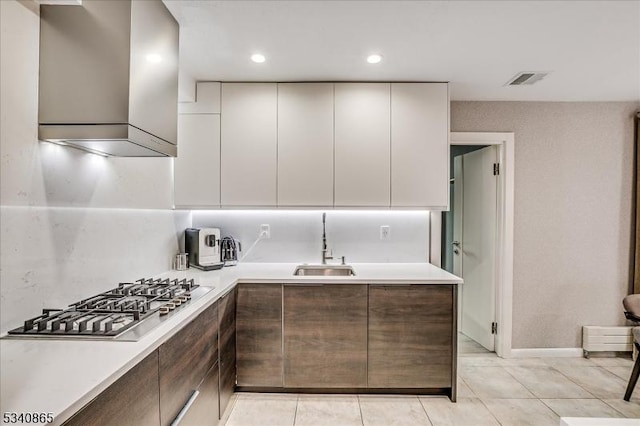 kitchen with stainless steel gas cooktop, light countertops, a sink, modern cabinets, and wall chimney exhaust hood