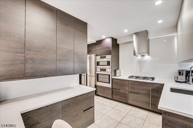 kitchen featuring light tile patterned floors, light countertops, wall chimney range hood, appliances with stainless steel finishes, and modern cabinets