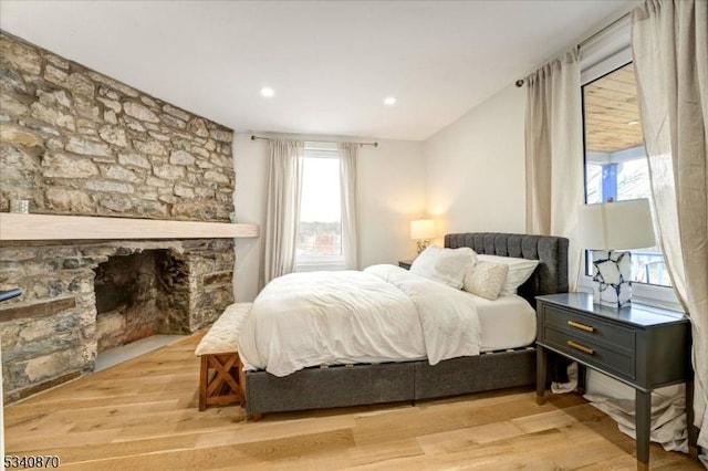 bedroom with wood finished floors and a stone fireplace