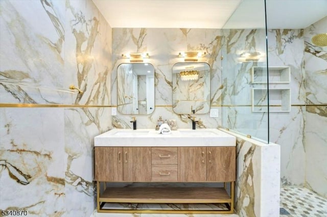 full bathroom with double vanity, a marble finish shower, tile walls, and a sink