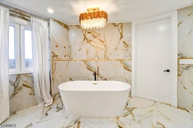 bathroom with marble finish floor, stone wall, and a soaking tub