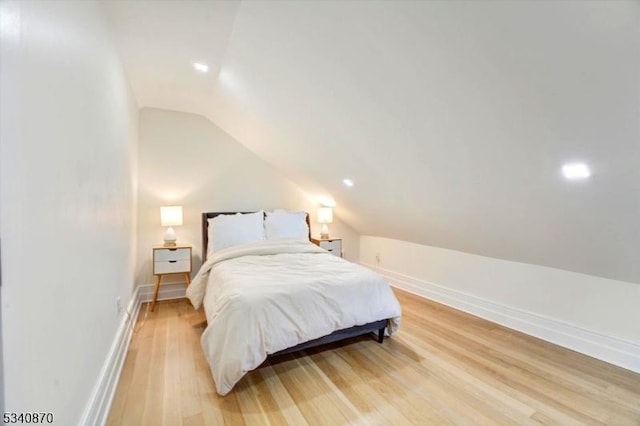 bedroom with vaulted ceiling, light wood finished floors, and baseboards