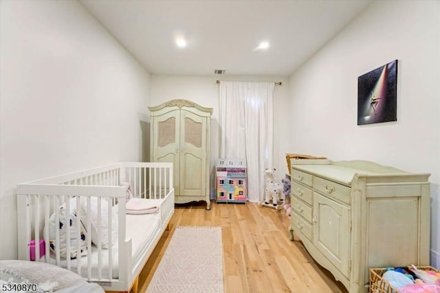 bedroom with light wood-type flooring, visible vents, and a crib