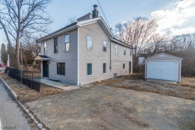 view of side of home with a chimney, a detached garage, fence, and an outdoor structure