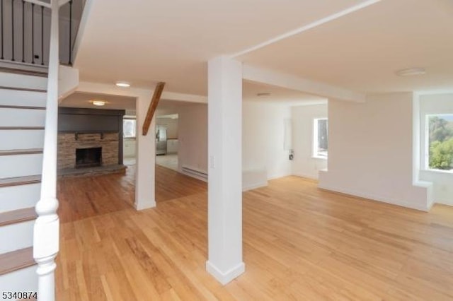 unfurnished living room featuring stairs, baseboard heating, a fireplace, and light wood-style floors