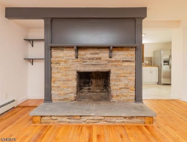 details with stainless steel fridge, baseboards, wood finished floors, a stone fireplace, and a baseboard heating unit