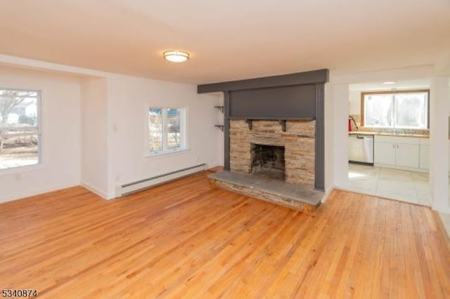 unfurnished living room featuring a stone fireplace, baseboard heating, light wood-type flooring, and a wealth of natural light