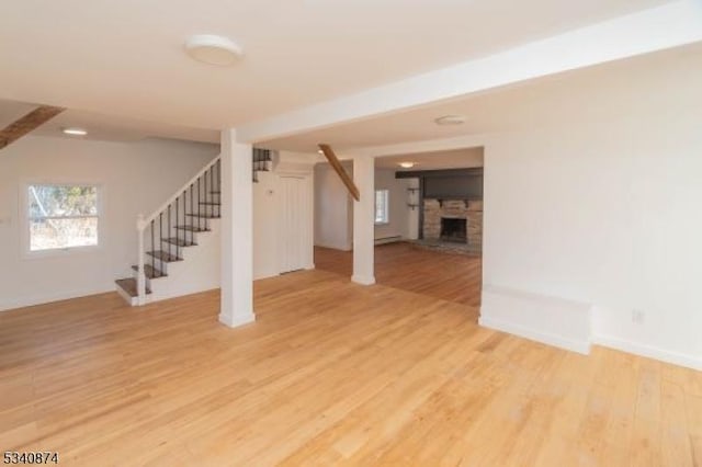 interior space with light wood-style flooring, a stone fireplace, stairway, and baseboards