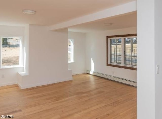 empty room with a healthy amount of sunlight, a baseboard radiator, and light wood-style flooring