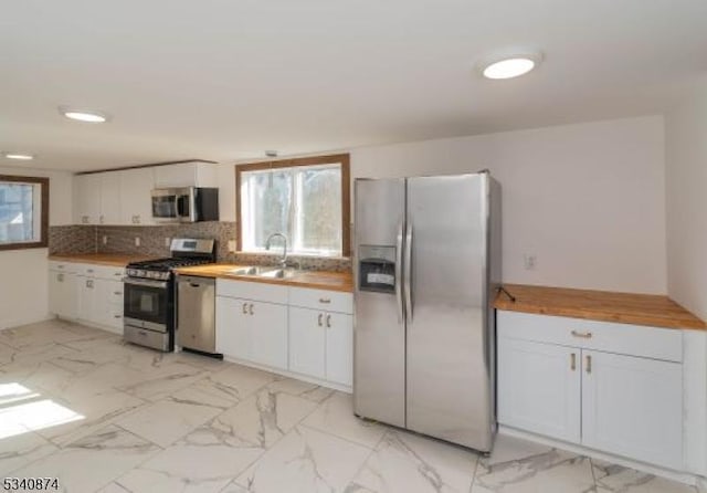 kitchen with marble finish floor, tasteful backsplash, appliances with stainless steel finishes, white cabinets, and a sink