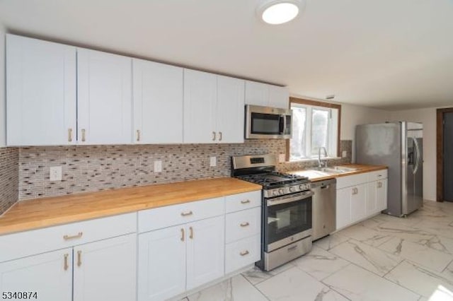 kitchen featuring marble finish floor, decorative backsplash, appliances with stainless steel finishes, white cabinetry, and a sink