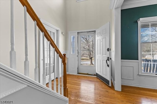 foyer featuring light wood-style floors, stairway, a decorative wall, and wainscoting