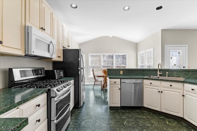 kitchen featuring stainless steel appliances, lofted ceiling, dark countertops, recessed lighting, and a sink