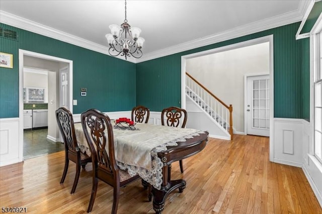 dining space featuring wainscoting, light wood-style flooring, stairway, crown molding, and a notable chandelier