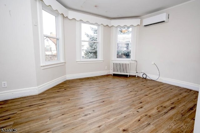 unfurnished room featuring radiator heating unit, baseboards, wood finished floors, and a wall mounted air conditioner