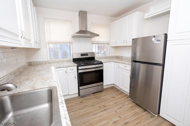 kitchen featuring appliances with stainless steel finishes, white cabinetry, a sink, and wall chimney exhaust hood