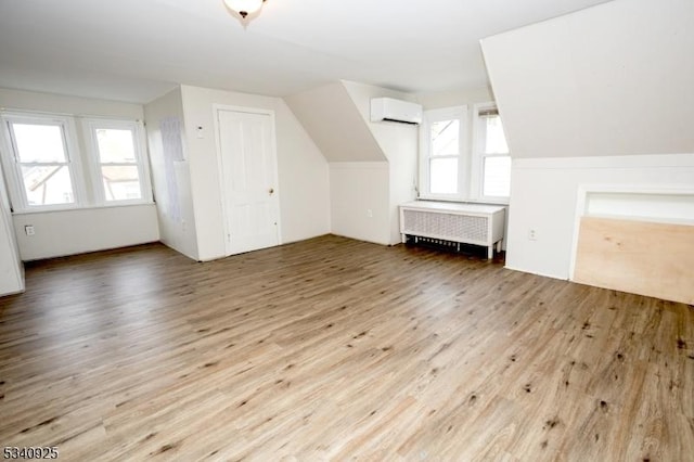 additional living space with lofted ceiling, a wall unit AC, radiator heating unit, and wood finished floors