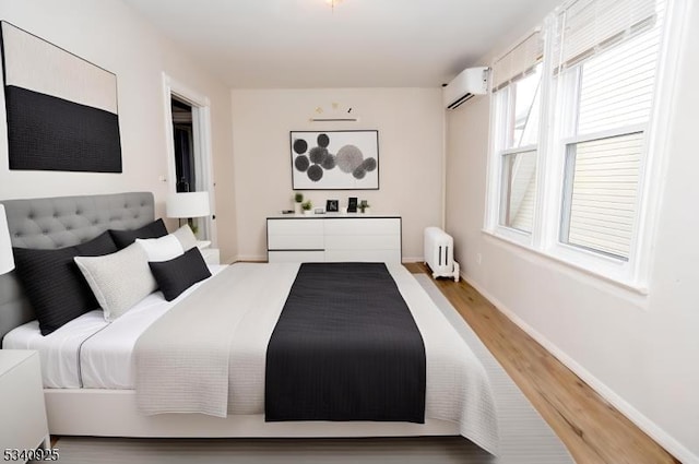 bedroom with a wall unit AC, radiator, baseboards, and wood finished floors