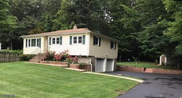 view of front of home featuring an attached garage, aphalt driveway, a chimney, and a front yard