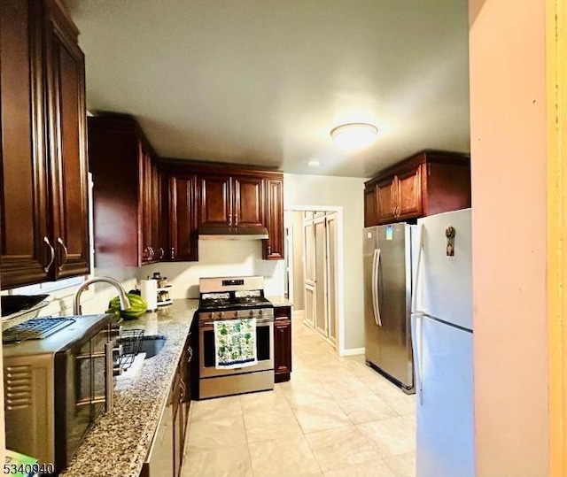 kitchen with under cabinet range hood, appliances with stainless steel finishes, a sink, and light stone countertops