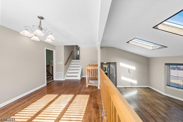 interior space with vaulted ceiling with skylight, visible vents, baseboards, and wood finished floors