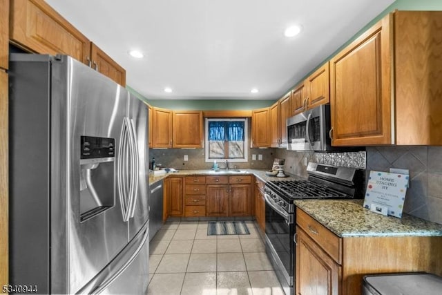 kitchen featuring stainless steel appliances, light stone counters, brown cabinetry, and a sink