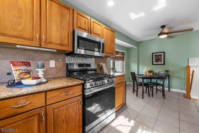 kitchen with light tile patterned floors, tasteful backsplash, baseboards, brown cabinets, and stainless steel appliances