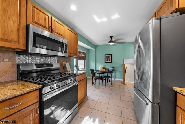 kitchen with light tile patterned floors, brown cabinetry, decorative backsplash, ceiling fan, and appliances with stainless steel finishes