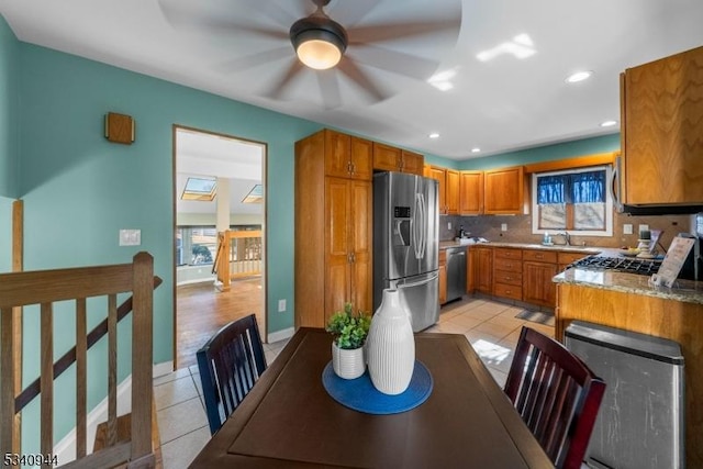 kitchen featuring brown cabinets, light tile patterned floors, stainless steel appliances, and a sink