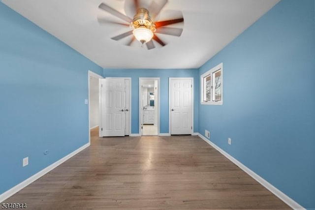 unfurnished bedroom featuring a ceiling fan, connected bathroom, baseboards, and wood finished floors