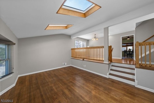 unfurnished room with a notable chandelier, vaulted ceiling with skylight, baseboards, and wood finished floors