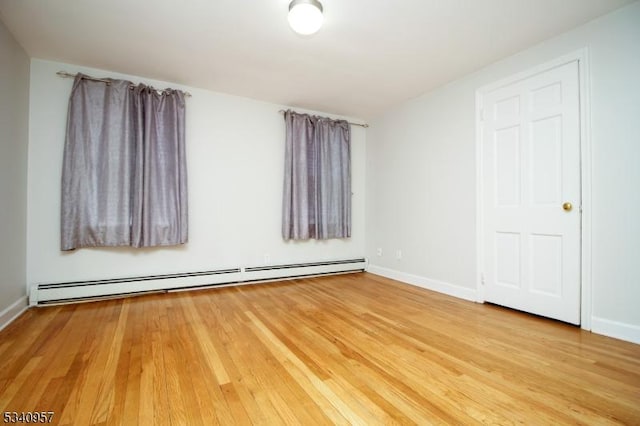 unfurnished room featuring baseboards, a baseboard heating unit, and wood finished floors