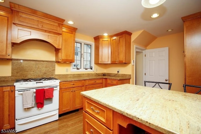 kitchen with brown cabinets, recessed lighting, light wood-style floors, light stone countertops, and white gas range oven