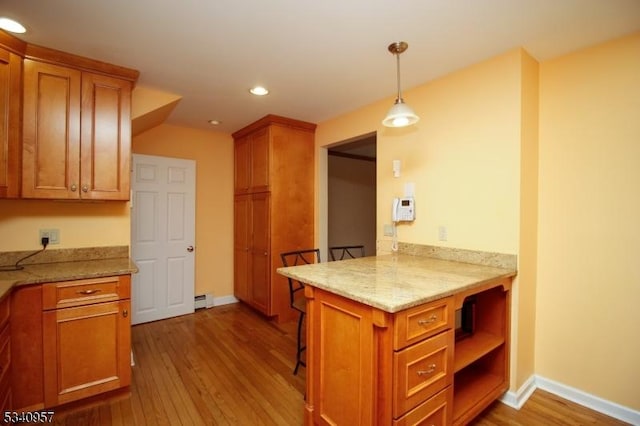 kitchen with recessed lighting, wood finished floors, hanging light fixtures, brown cabinets, and light stone countertops