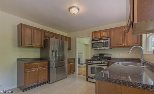 kitchen with baseboards, dark stone counters, appliances with stainless steel finishes, brown cabinets, and a sink