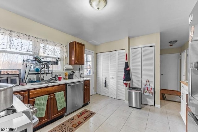 kitchen with light tile patterned floors, brown cabinetry, light countertops, stainless steel dishwasher, and a sink