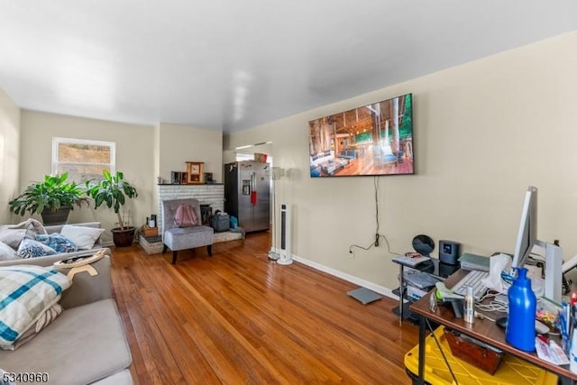 living room with a brick fireplace, baseboards, and wood finished floors