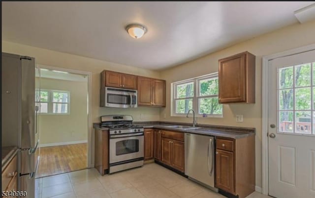 kitchen featuring a sink, appliances with stainless steel finishes, dark countertops, brown cabinetry, and plenty of natural light