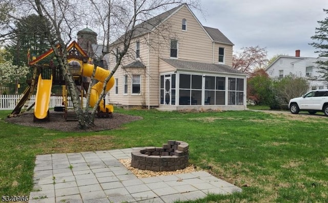 rear view of property with a sunroom, a playground, a yard, and an outdoor fire pit