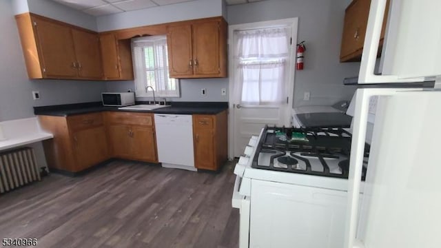 kitchen with brown cabinetry, a paneled ceiling, a sink, white appliances, and dark wood-type flooring