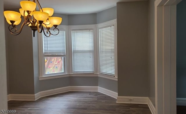 unfurnished dining area with an inviting chandelier, baseboards, plenty of natural light, and dark wood-type flooring