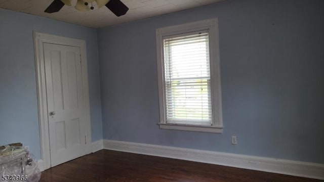 spare room with baseboards, a ceiling fan, dark wood-type flooring, and a wealth of natural light