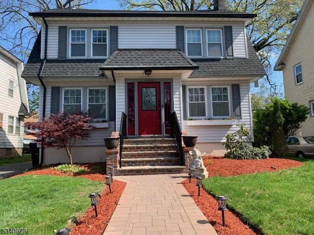 view of front of property featuring entry steps, roof with shingles, and a front yard