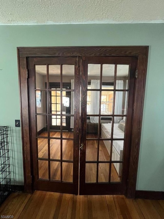 interior details with a textured ceiling, baseboards, wood finished floors, and french doors