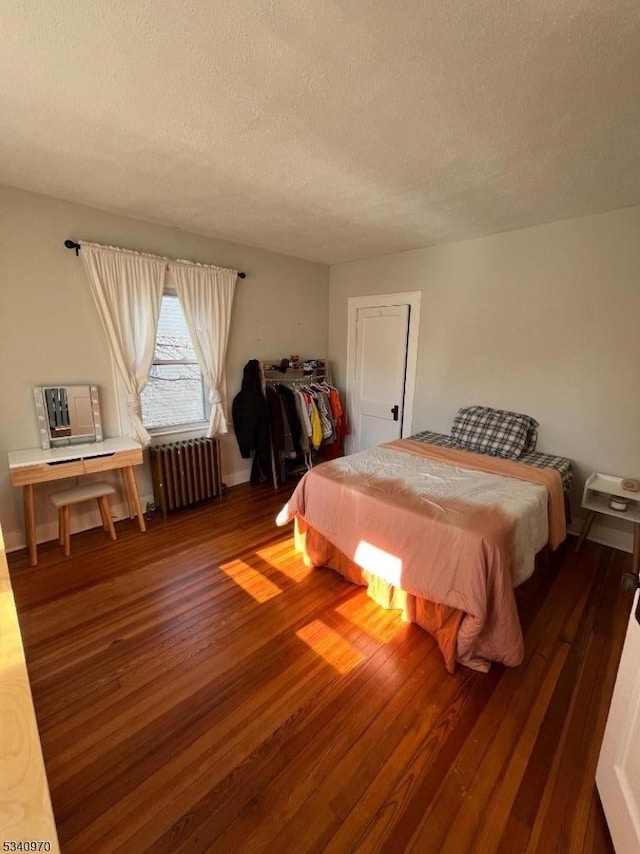 bedroom with hardwood / wood-style flooring, radiator heating unit, and a textured ceiling