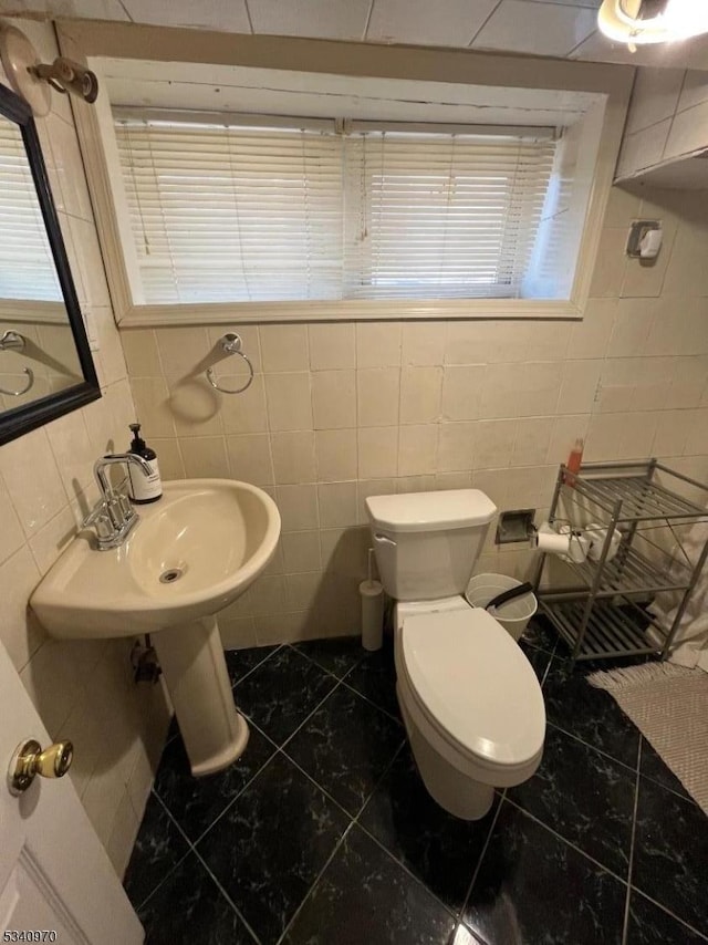 bathroom featuring a sink, toilet, and tile walls