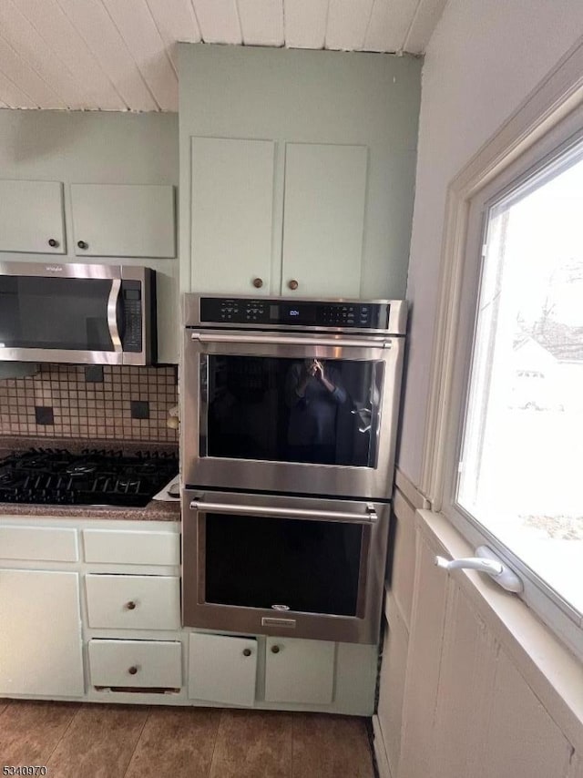 kitchen featuring appliances with stainless steel finishes, tile patterned floors, white cabinetry, and decorative backsplash