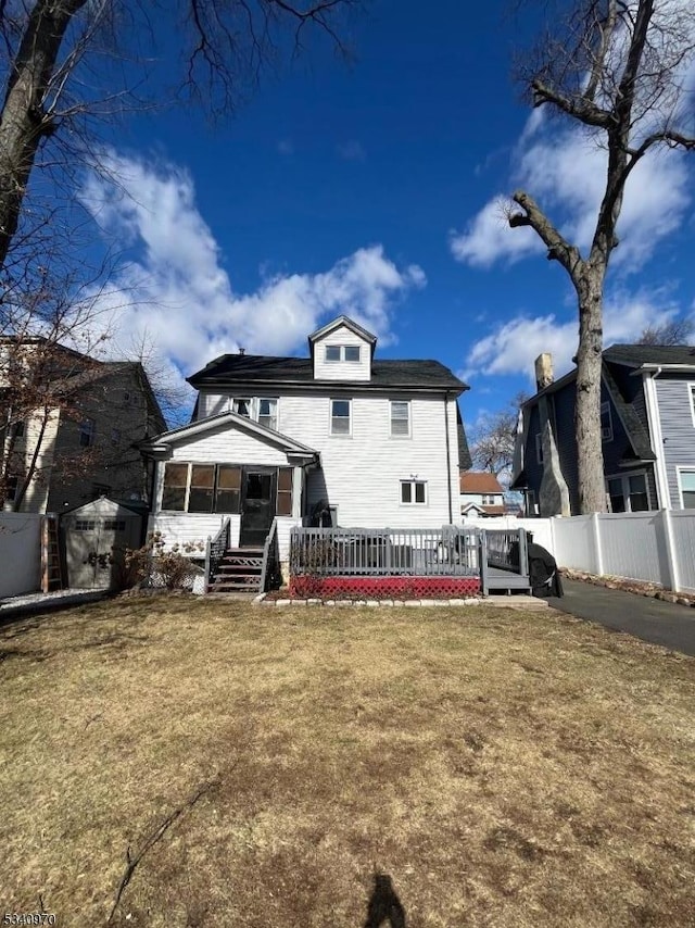 rear view of house featuring a sunroom, fence, an outdoor structure, and a yard