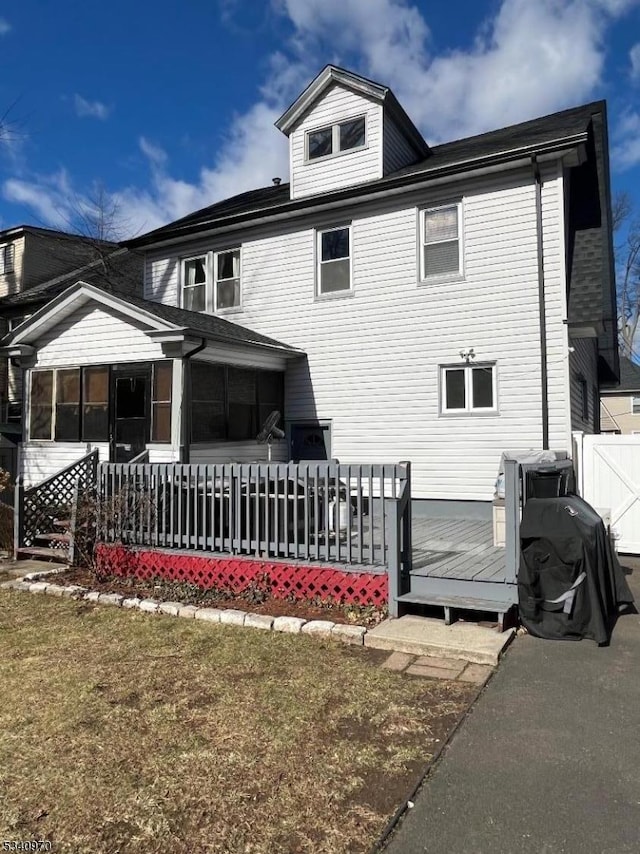 rear view of property featuring a yard, a sunroom, fence, and a deck